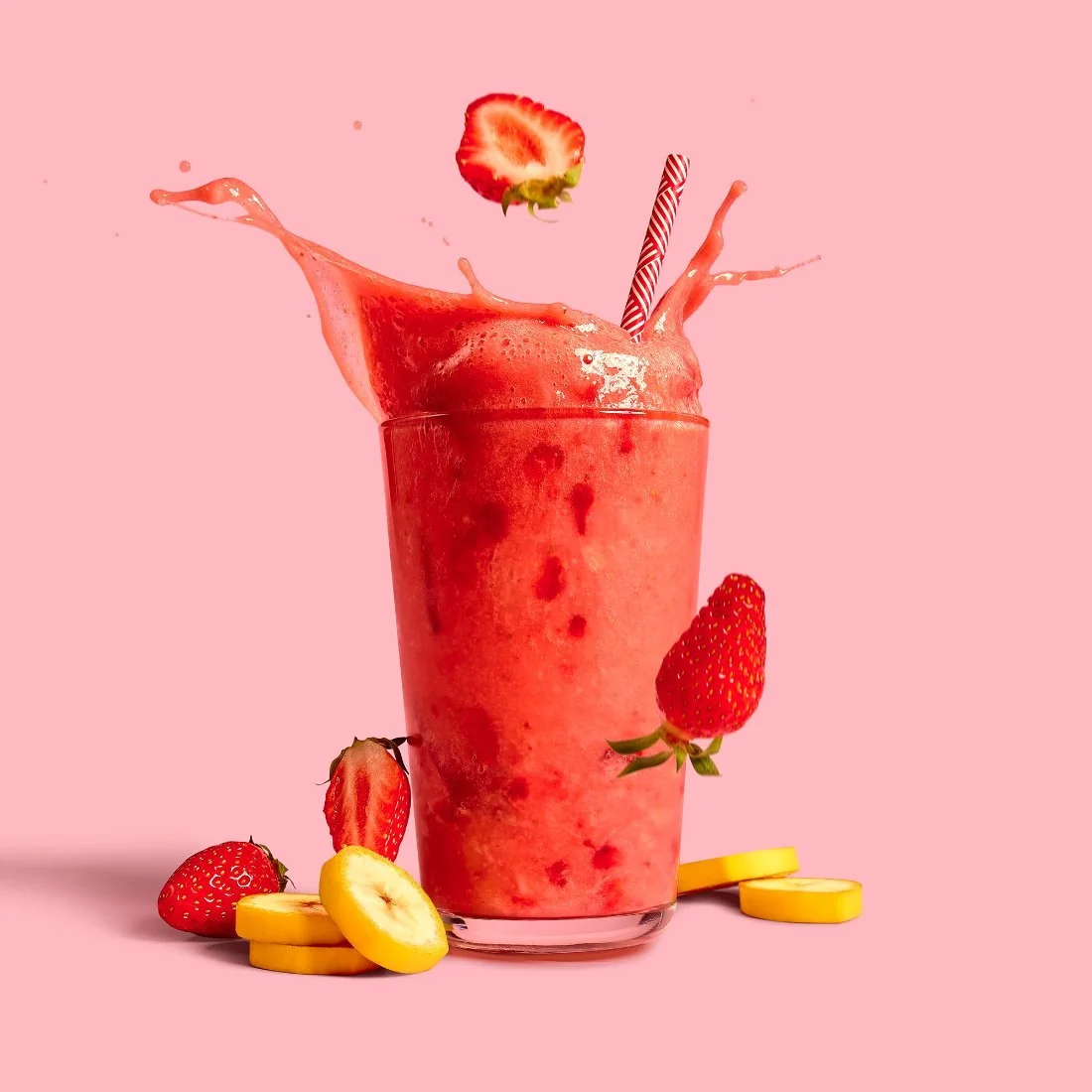 A strawberry smoothie splashing out of a glass, on a pink backdrop