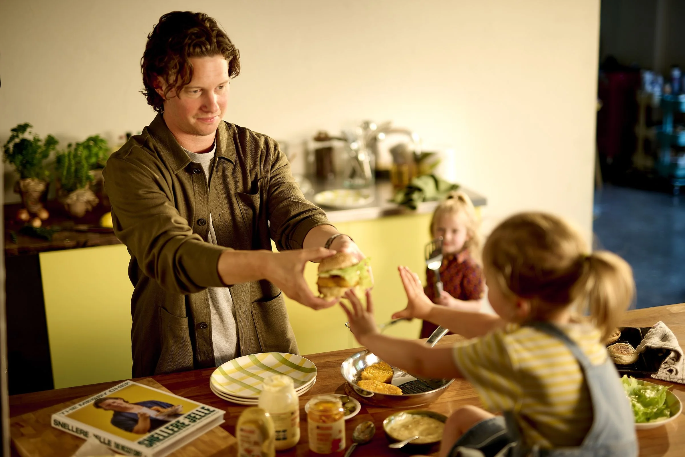 Close-up: a chef hands a burger to two children at a kitchen counter